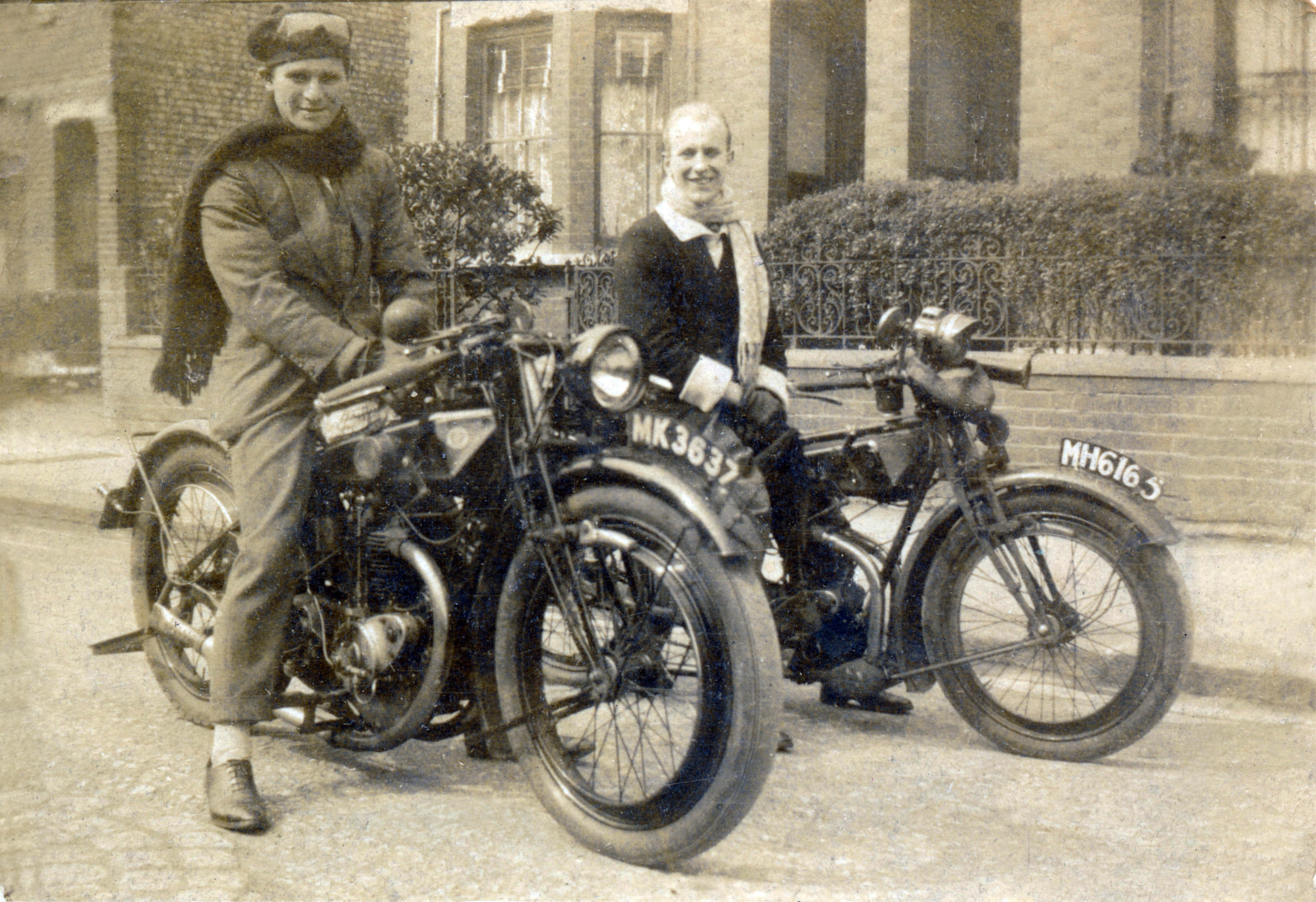 Two men with motorcycles in front of a building
