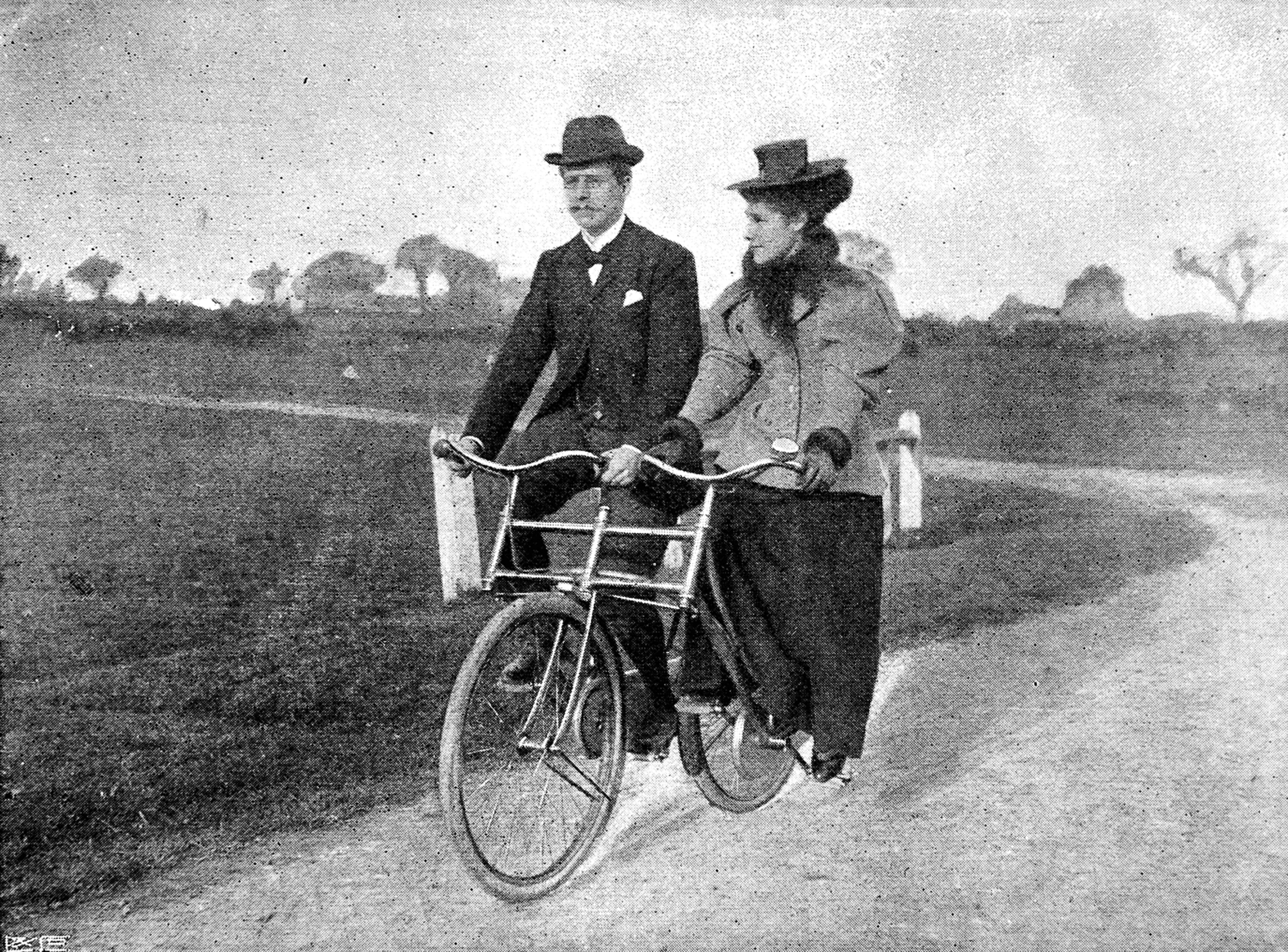 Two people riding a tandem bicycle on a road with a landscape in the background