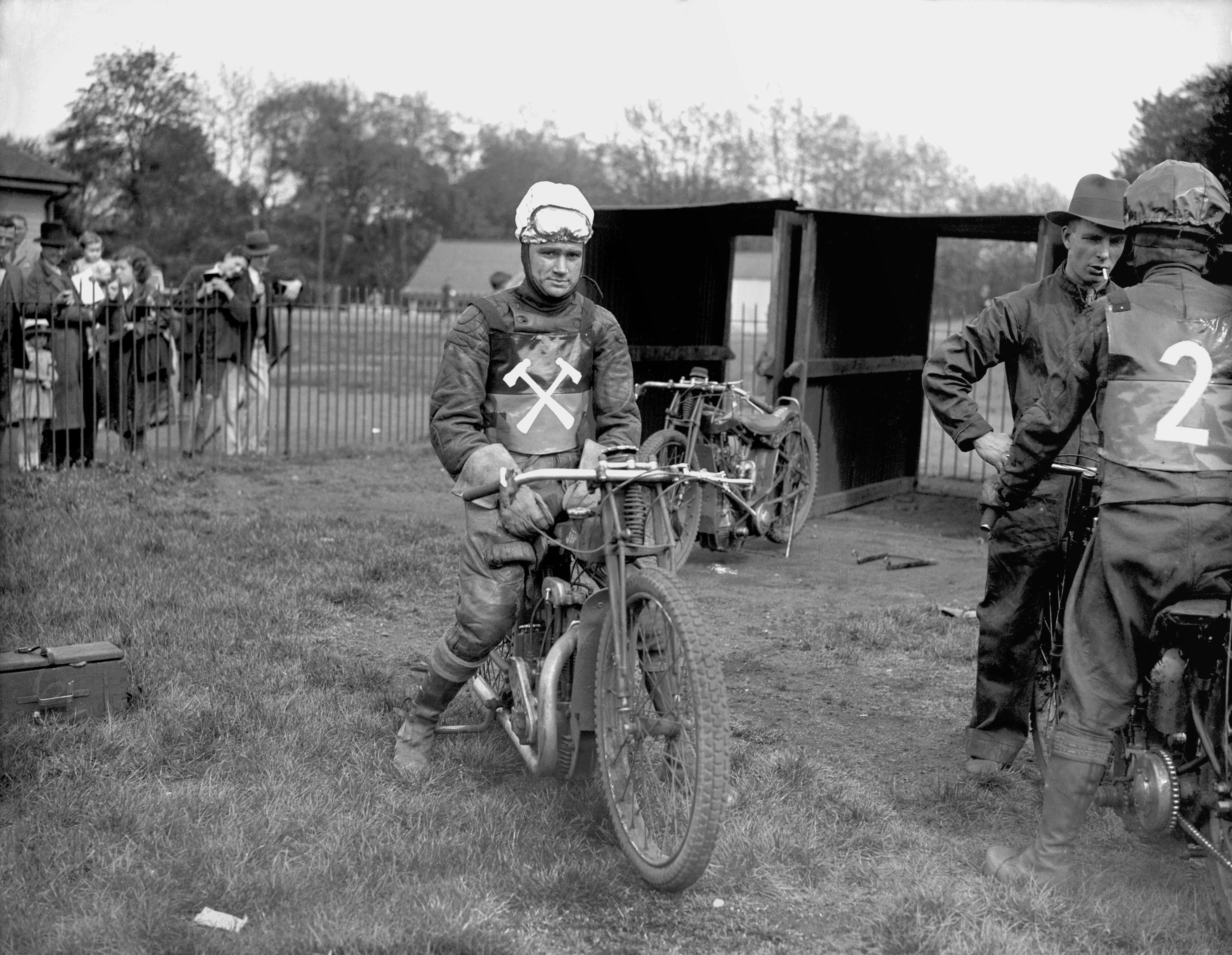 Two men on motorcycles with number 2 on a grassy area.