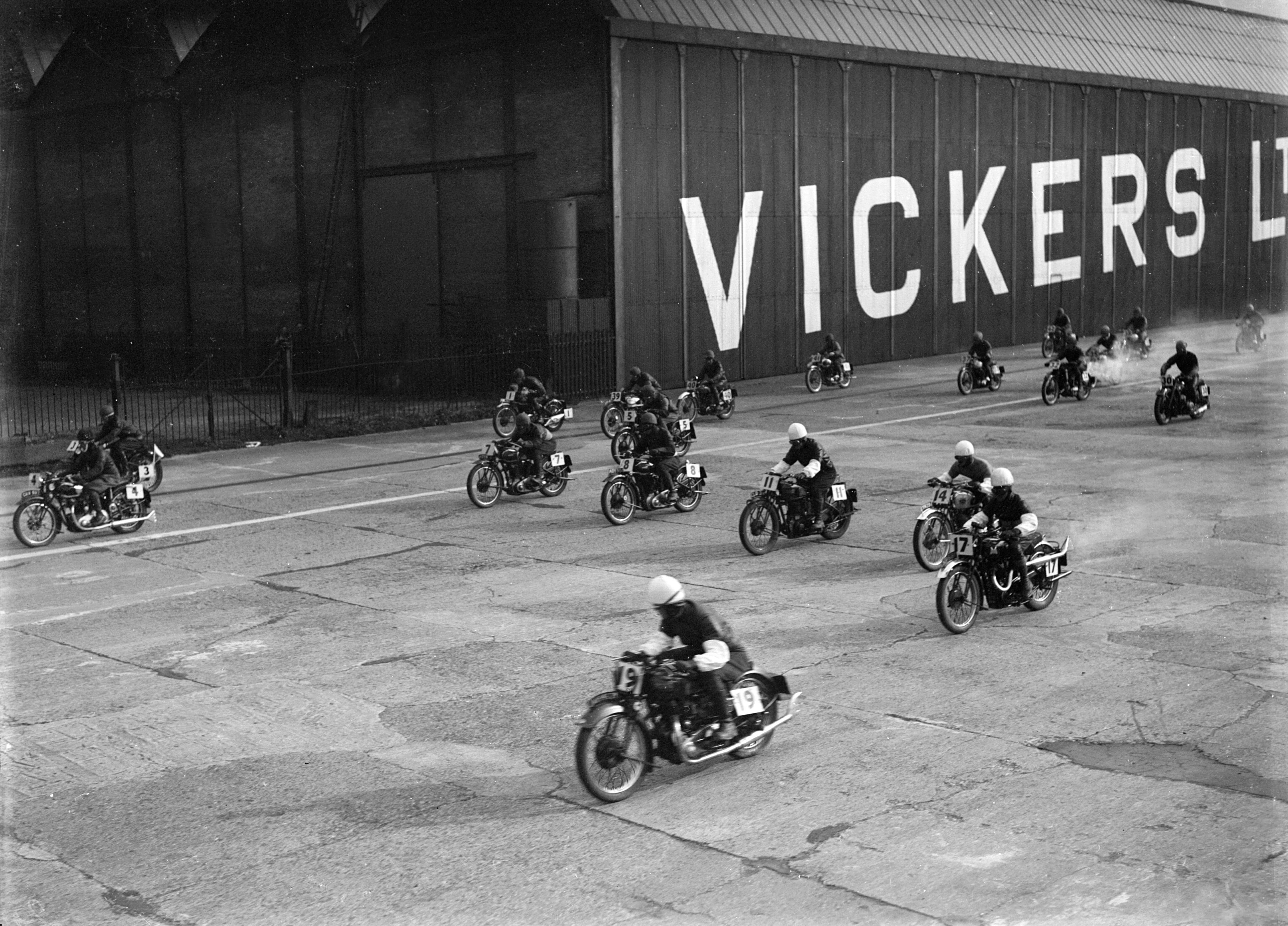Motorcycle riders on a track with 'Vickers' branding in the background