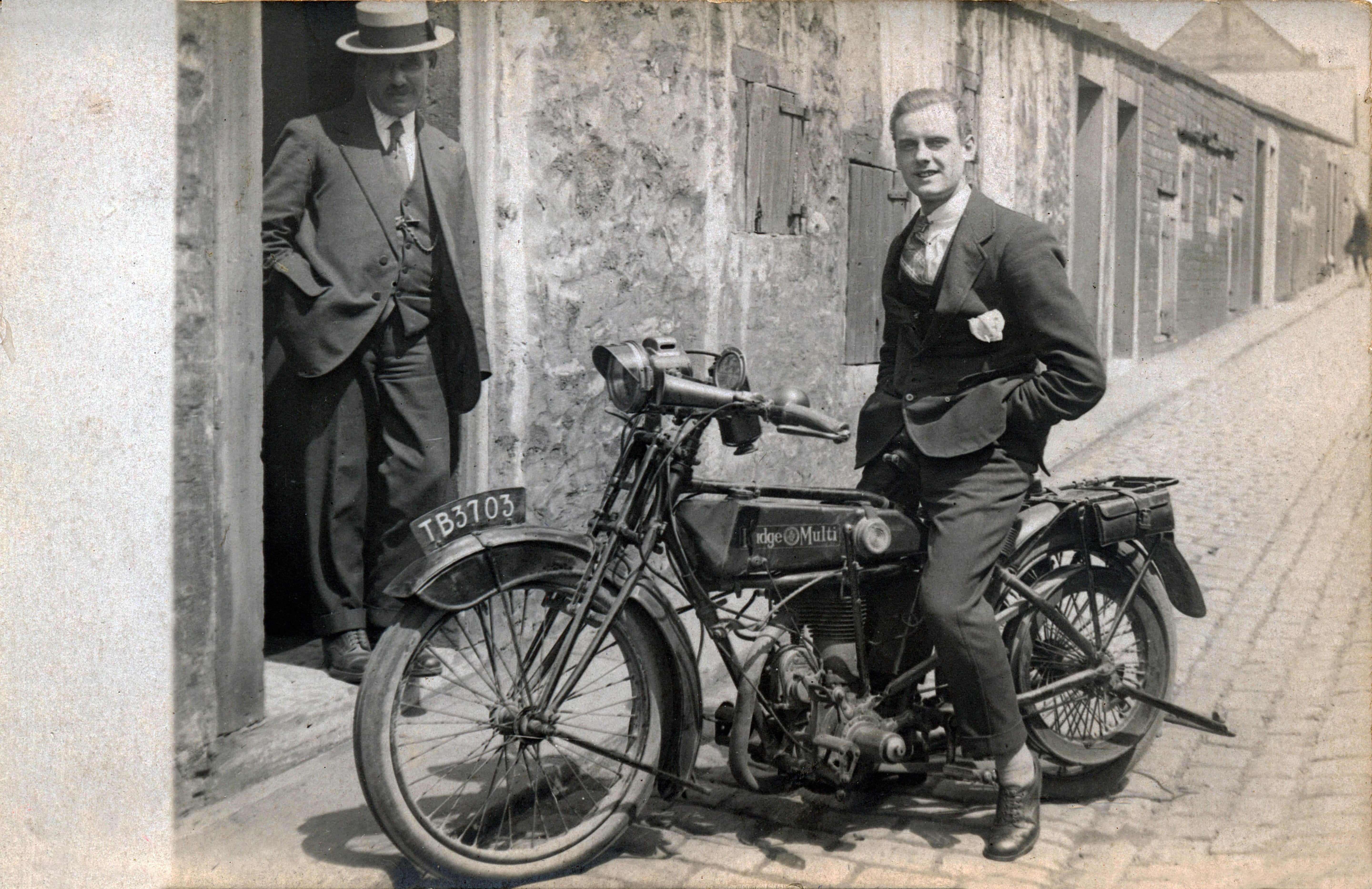 Two men with a vintage motorcycle on a street.